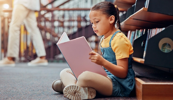 young girl reading a book while sitting on the floor